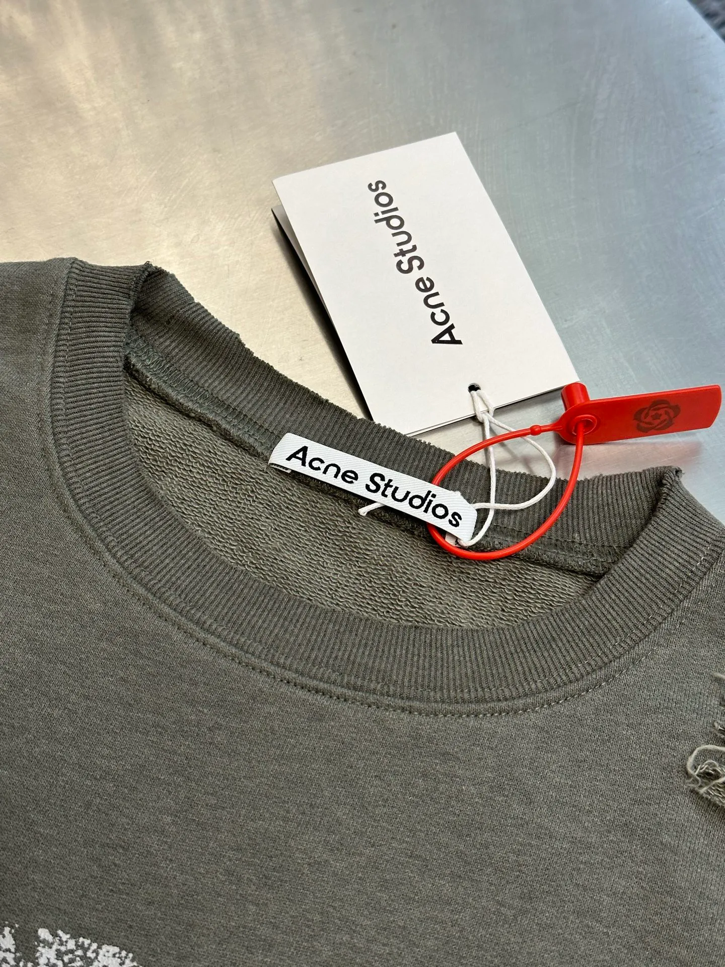 Ac Studios ripped distressed logo sweatshirt, custom dyed 1:1 gray green soft cotton sweatshirt material, the top fabric and terry bottom are the same color configuration, the market fabric In Stock has a different color on the top and bottom, which does not match the original! The minimum order quantity of fabric is 2 tons, and the fabric manufacturing process alone takes 45 days! The unruly soul of Ac Studios is engraved on the chest. The ingenious integration of hole elements and wanton swaying on the Gray canvas is a deliberate rebellion and a break away from the shackles of tradition. It is unique in the wave of the trend. It uses glue printing. The chest printing has been modified three times with the film screen. The glue liquid paint is used to print the pattern on the fabric, and the fabric is baked to fix the printing pattern. Many parts of the body of the garment are frayed and worn at regular intervals by purely artificial means, and marks are manually brushed to add texture and depth to the surface of the garment to imitate the texture of natural wear and tear. size：s m l xl